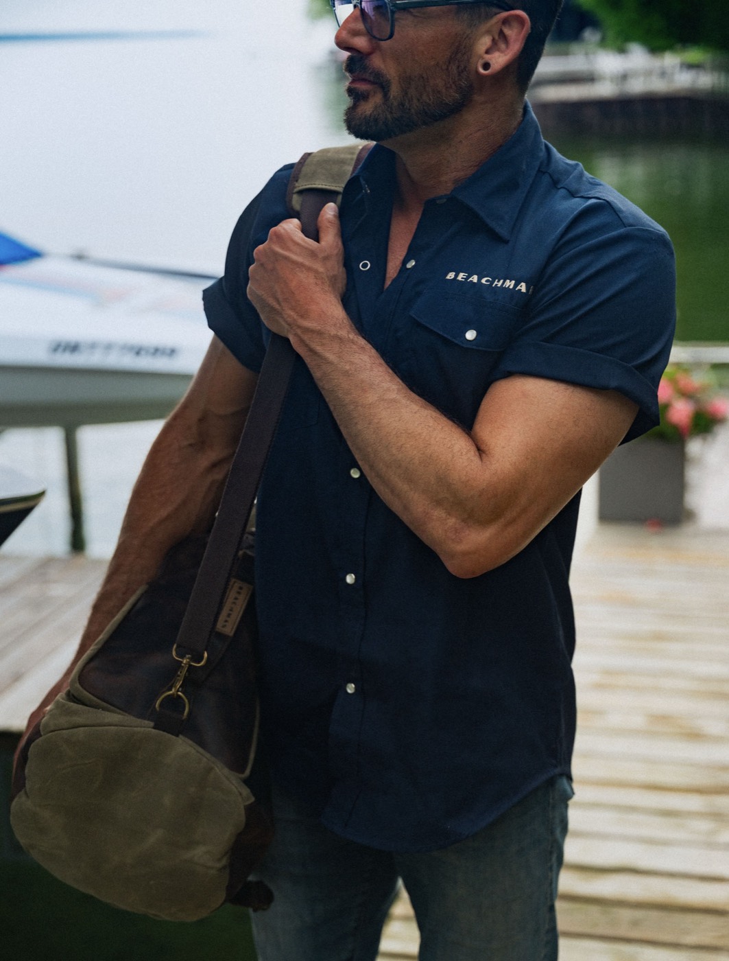 Beachman apparel — model in a blue tee carrying a waxed canvas bag at a dock