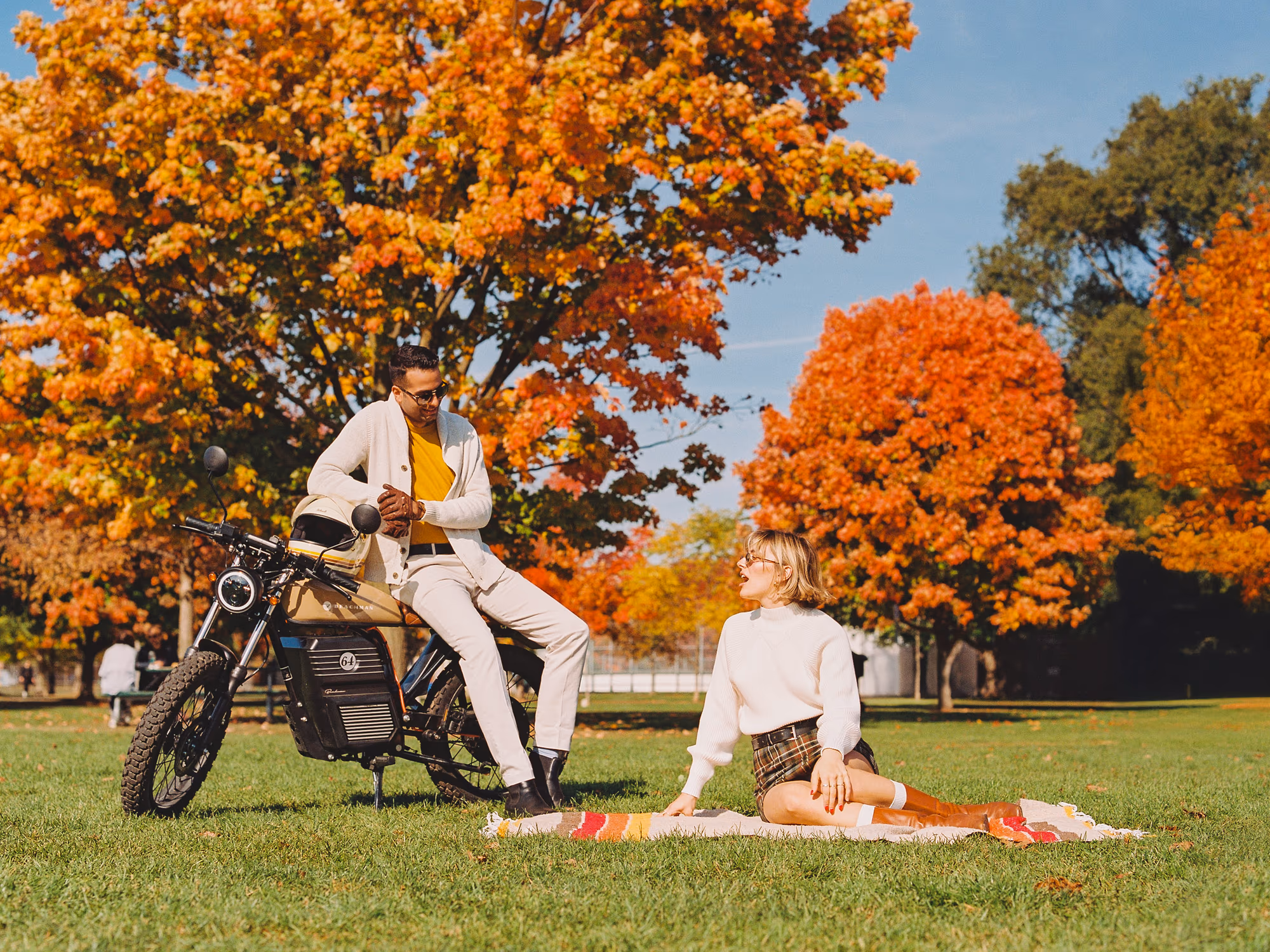 A couple beside an electric motorbike under blazing autumn trees, shot on warm film