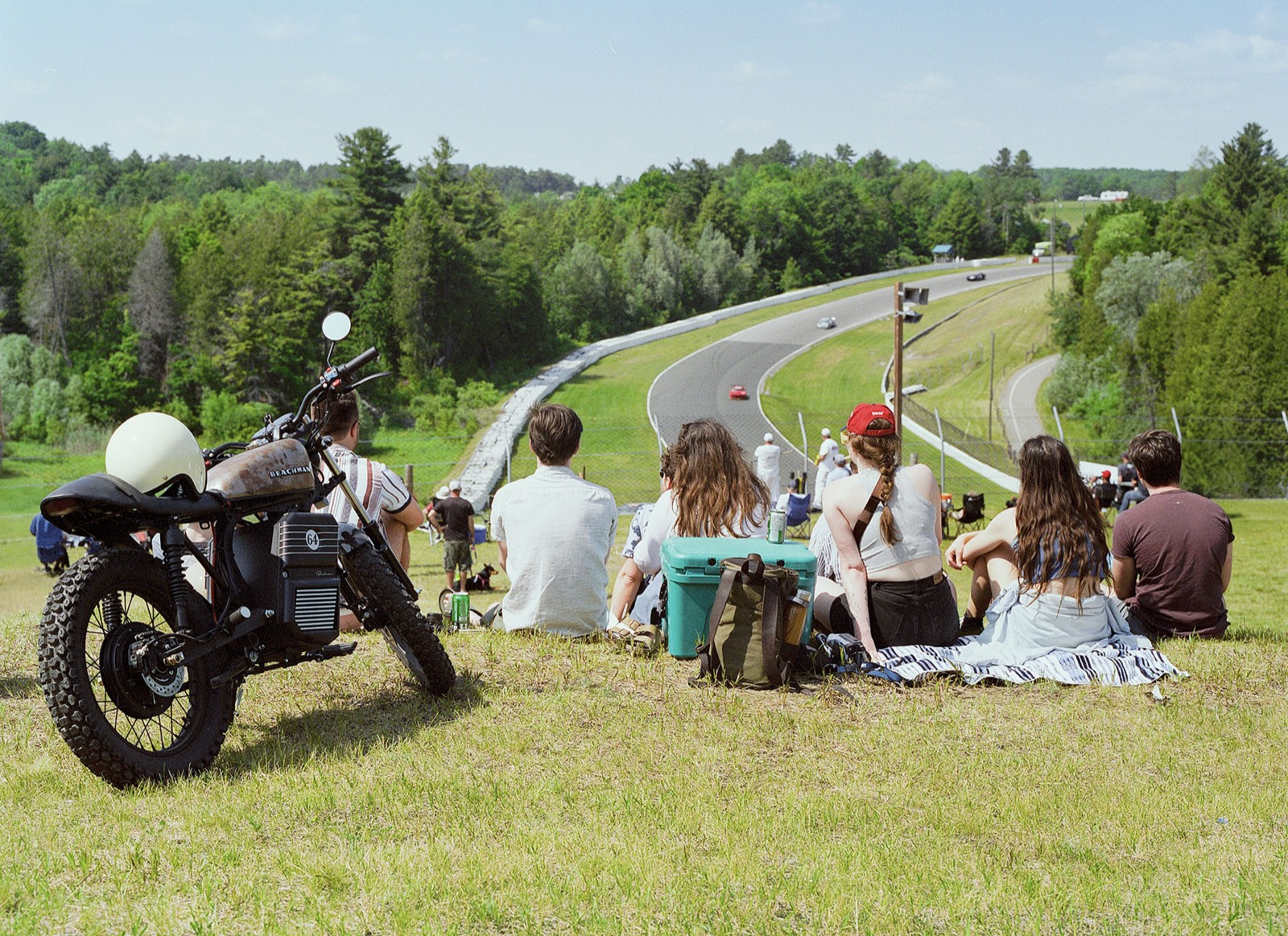 Friends sitting on a grassy hill overlooking a racetrack on film
