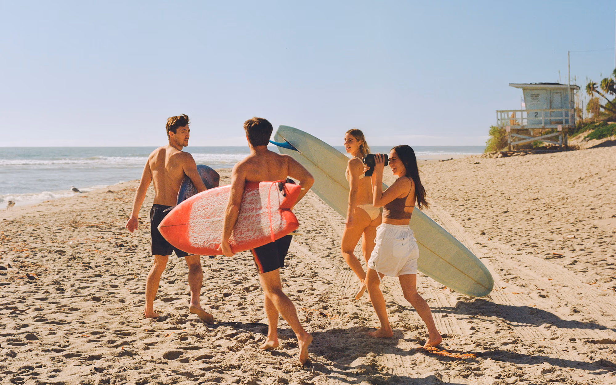 Three friends carrying surfboards across the sand past the lifeguard tower
