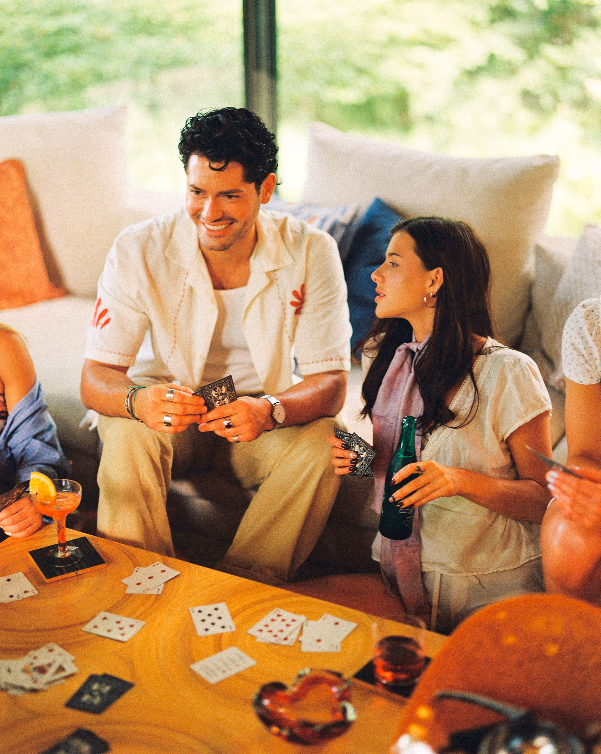 A couple playing cards over drinks at a warm living-room table