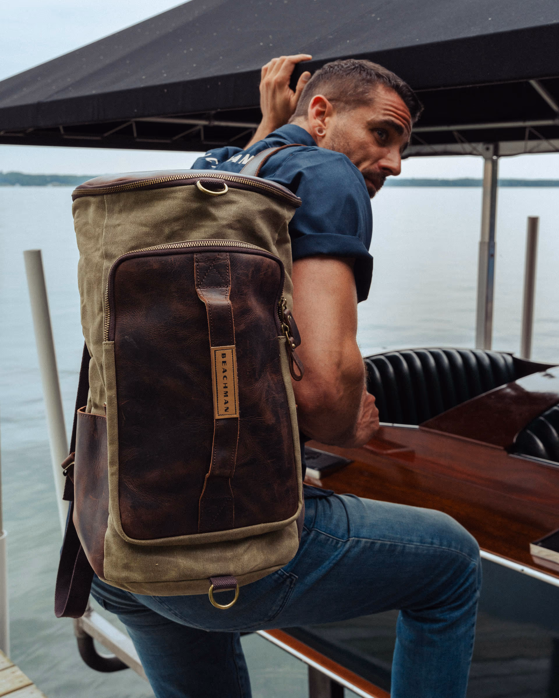 A man on a dock wearing the Beachman waxed-canvas duffel on his back