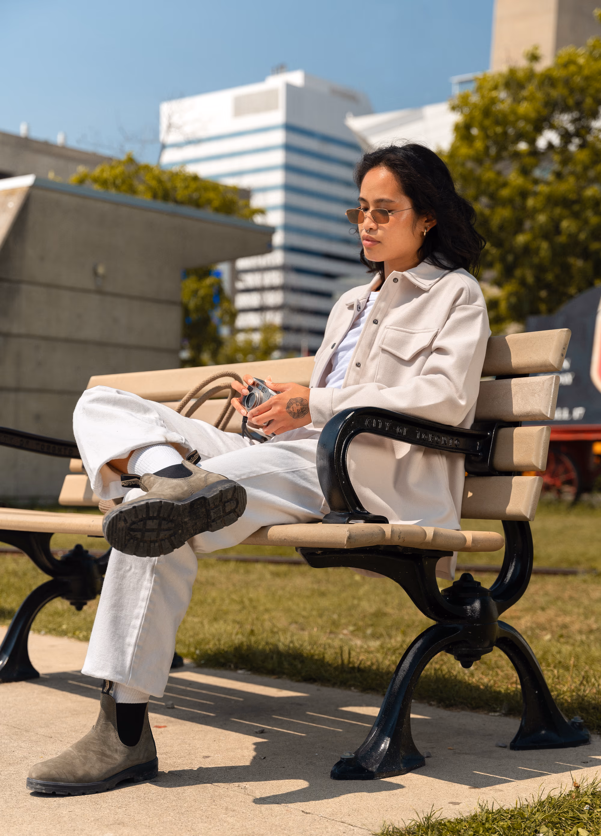 Seated on a park bench downtown, rustic-green Blundstones crossed