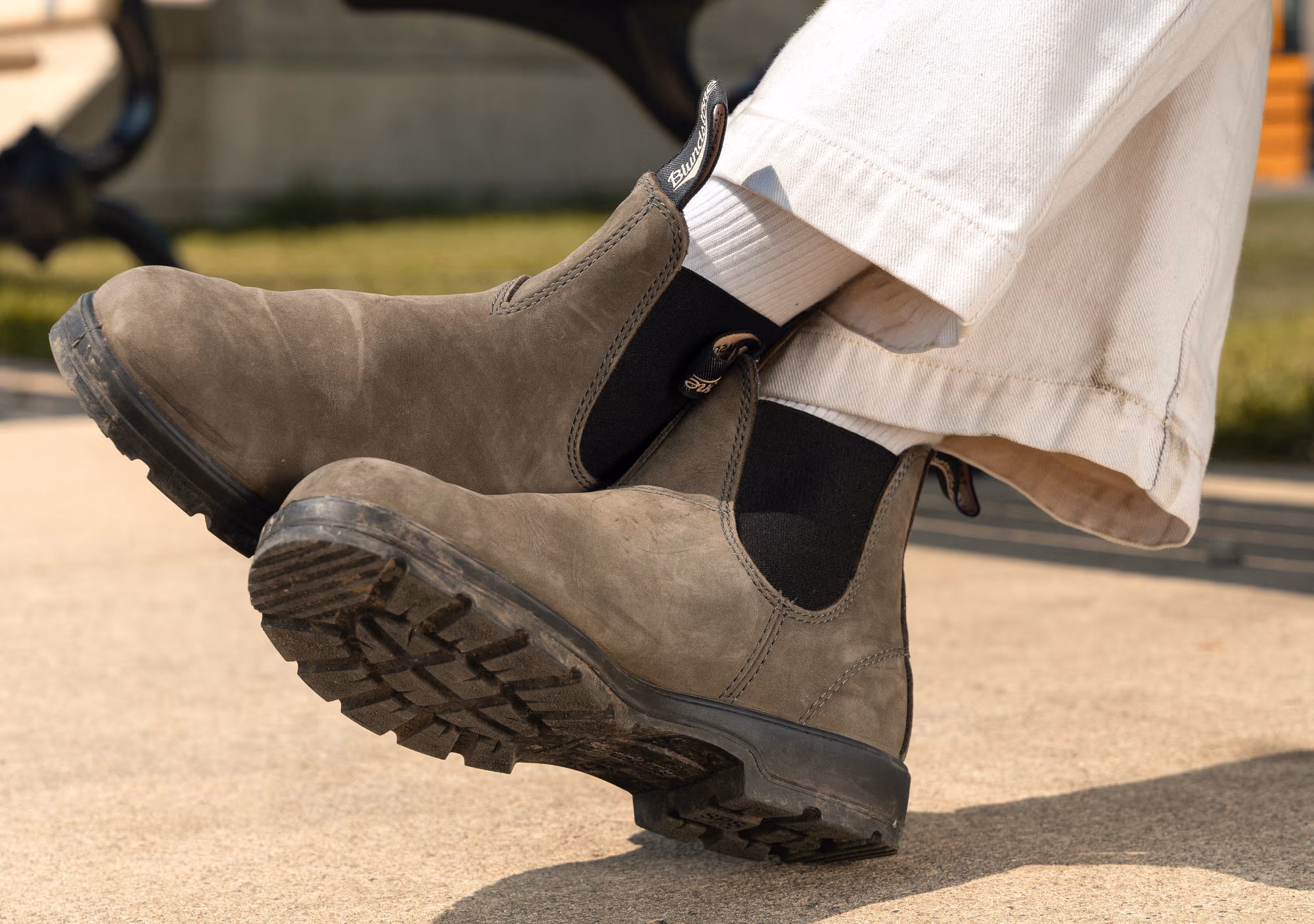 The olive suede Chelsea boots mid-stride against white trousers