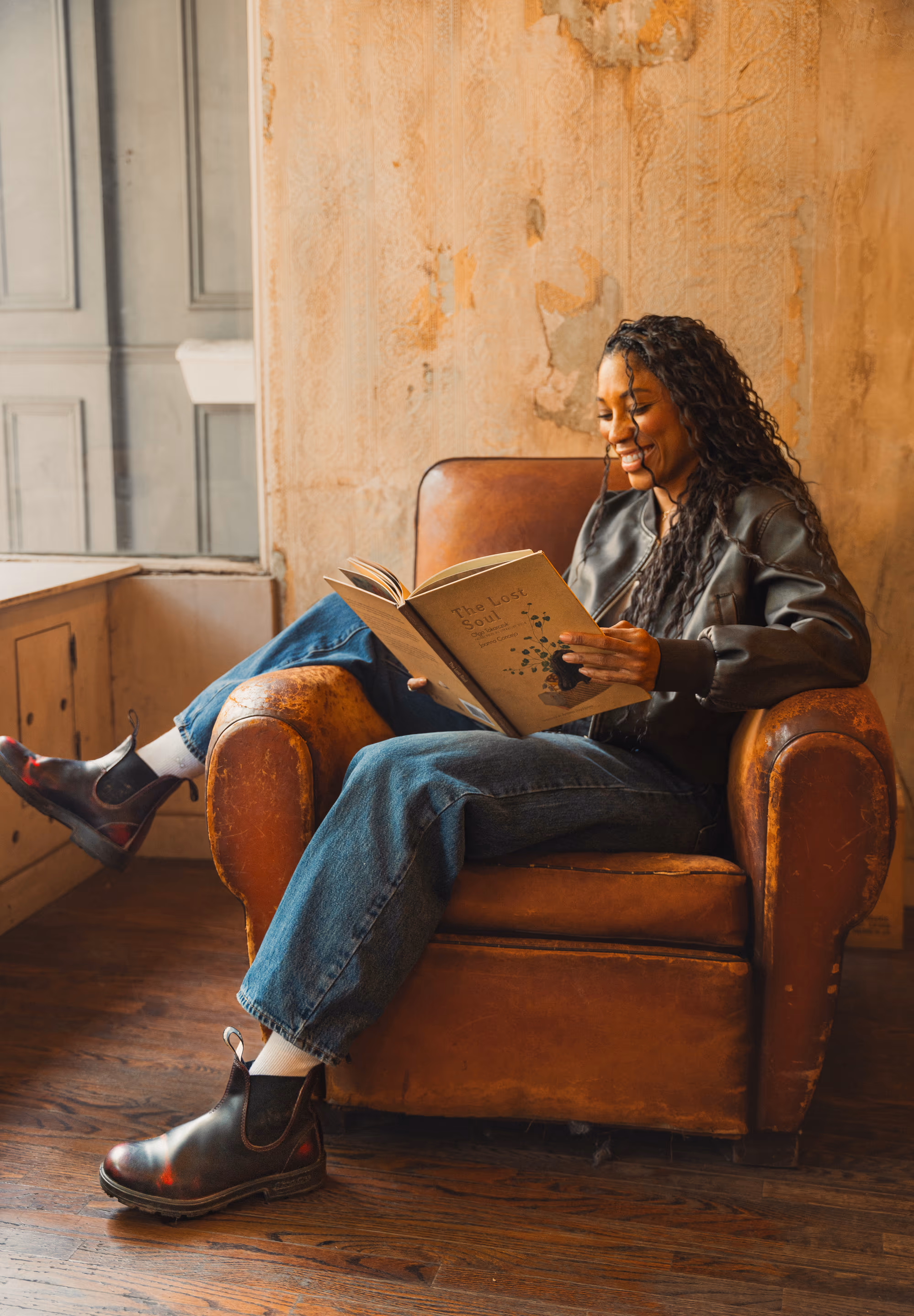 Reading in a leather armchair, dark-cherry Blundstones on