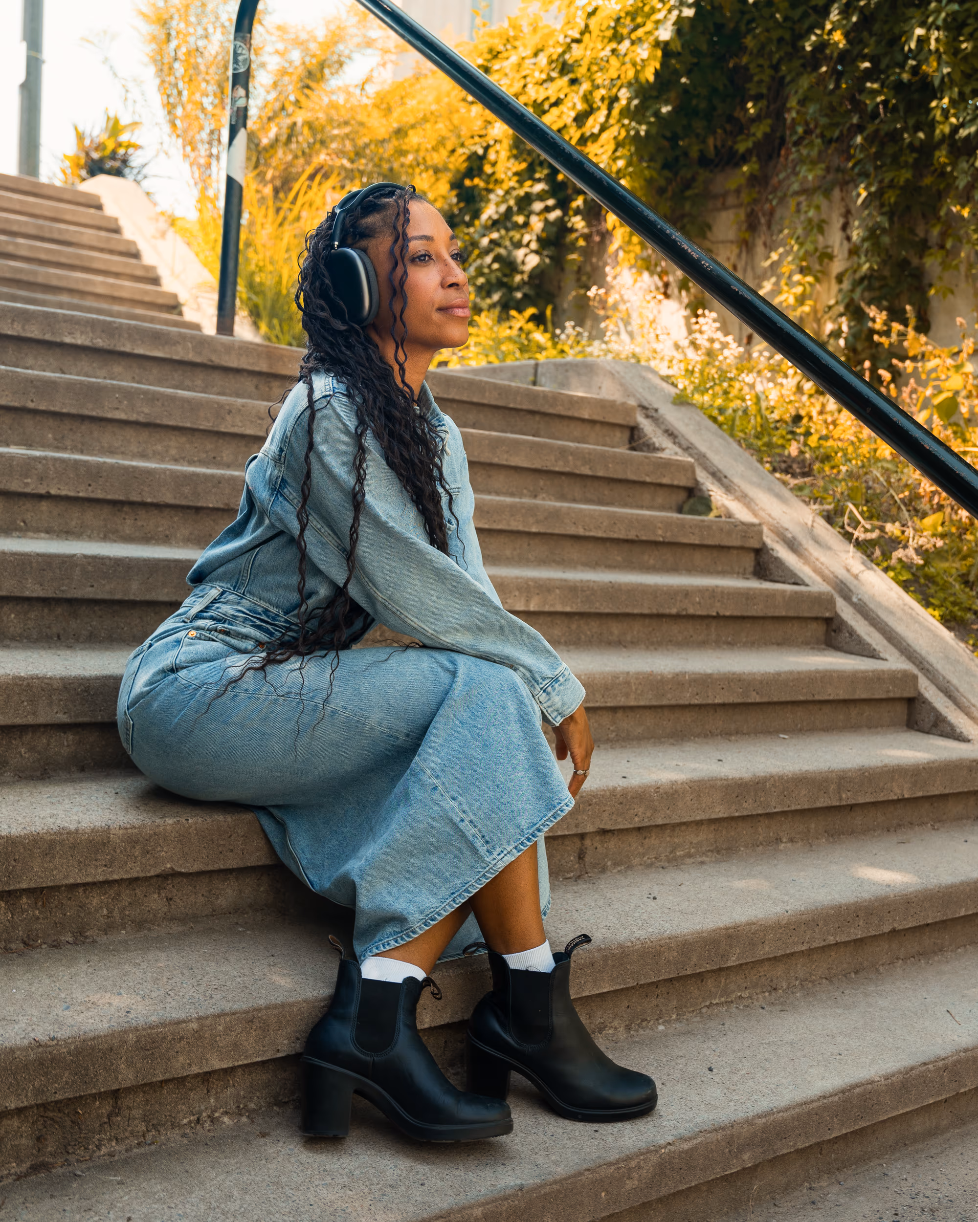 A woman in a denim dress and heeled black Blundstone Chelsea boots seated on outdoor steps