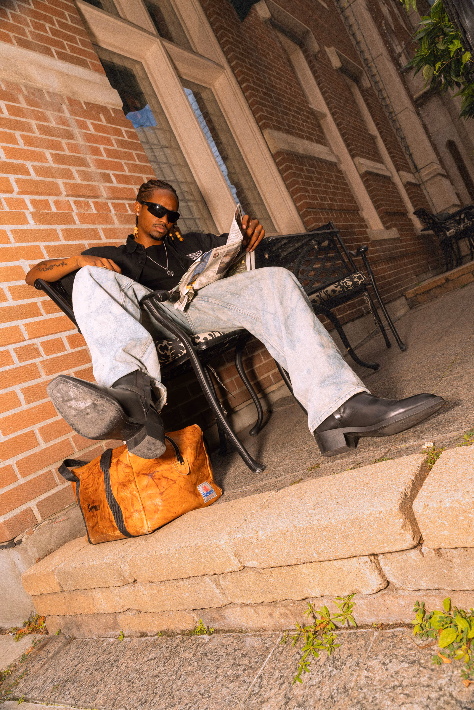 On the brick steps with a leather bag, reading