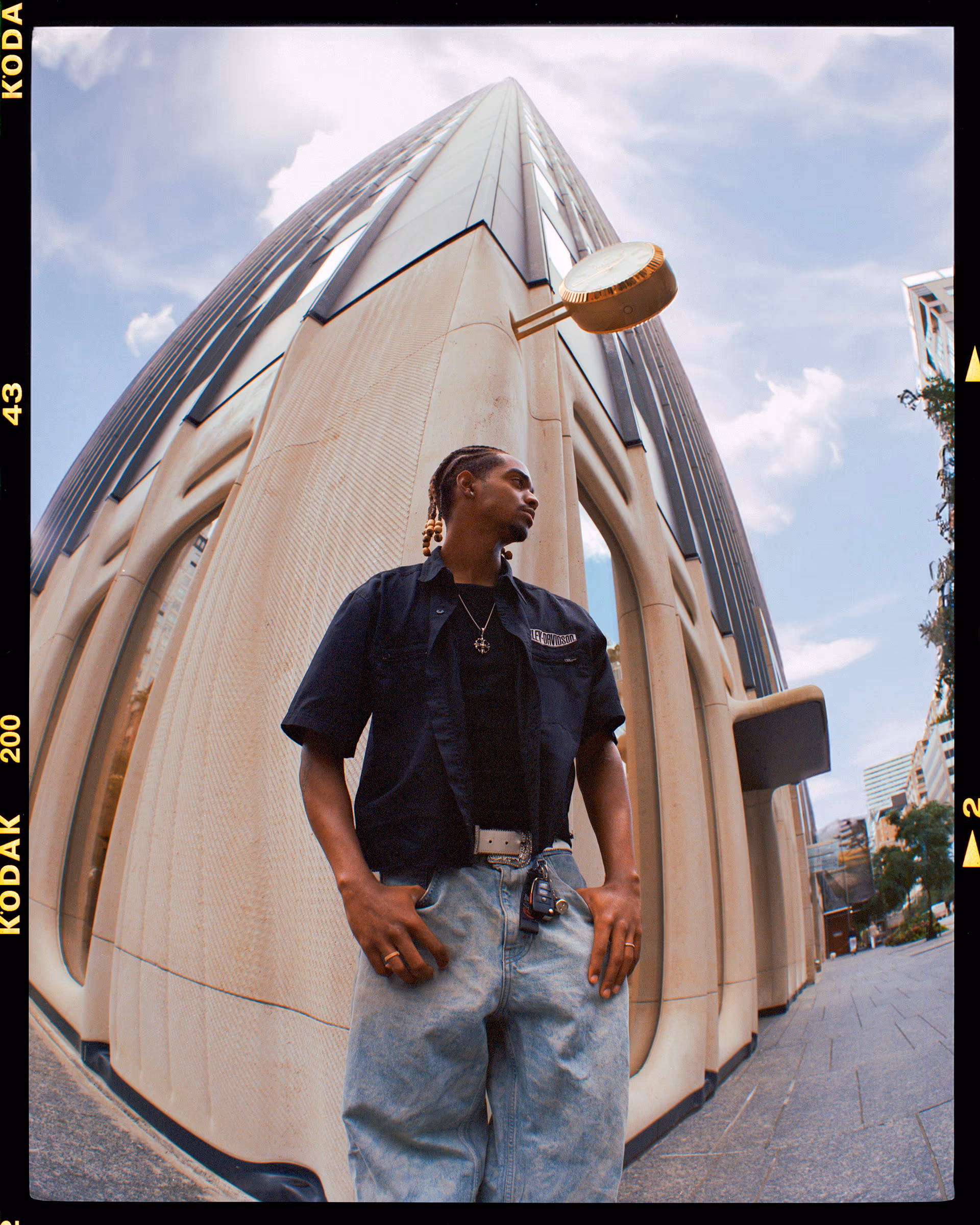 Samuel in a fisheye portrait outside a sculptural white building, shot on Kodak film