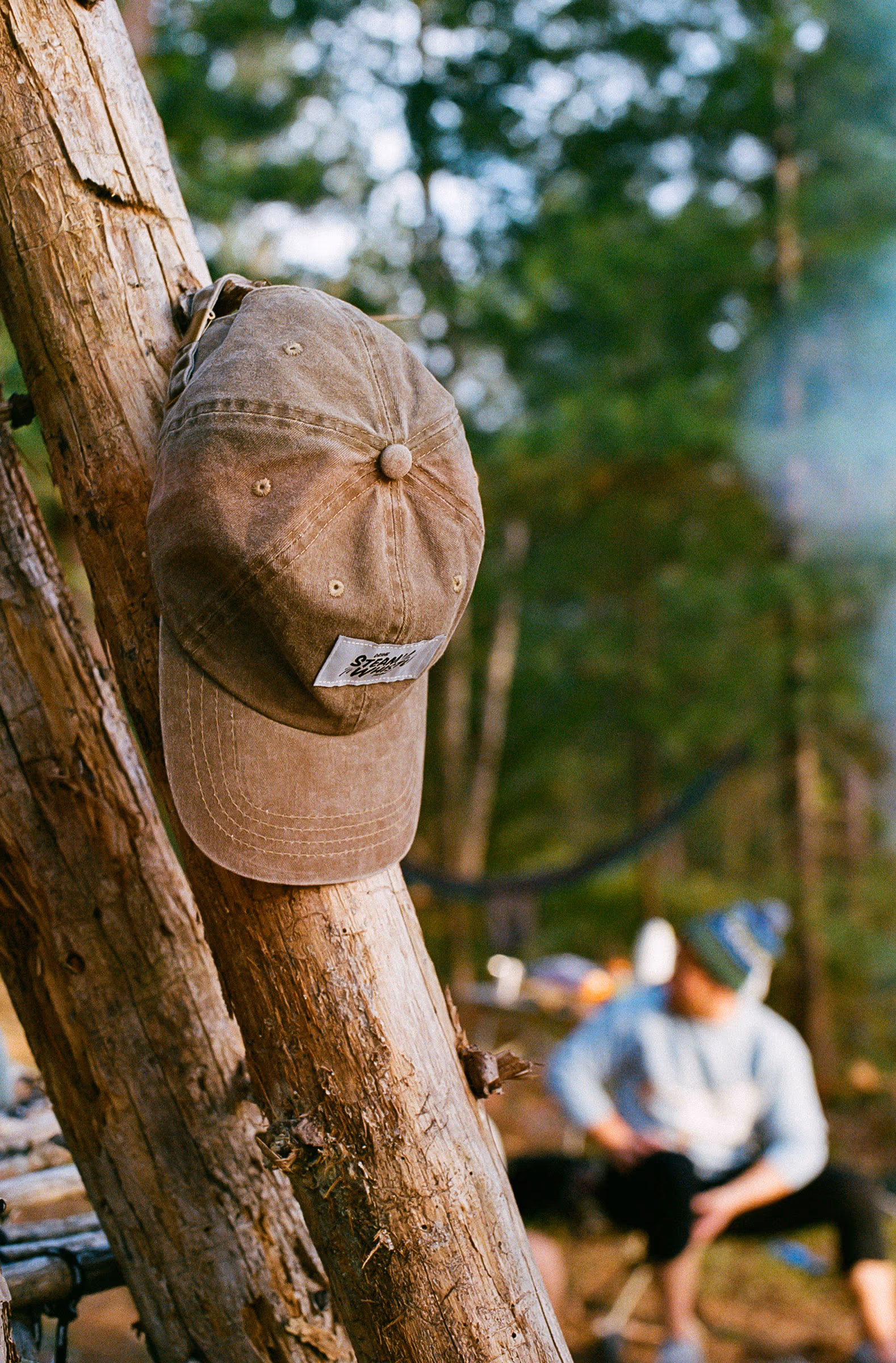 A ballcap hung on a branch, camp carrying on behind