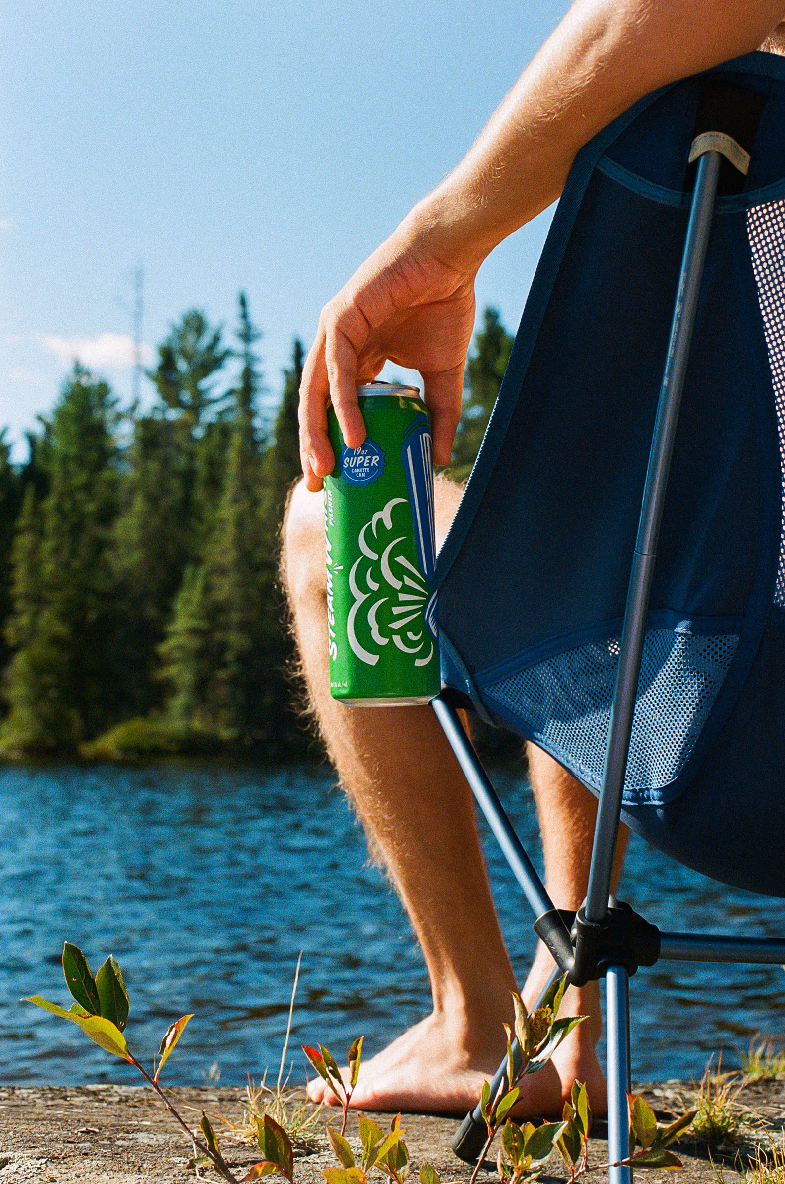 A can in hand at the water’s edge beside the camp chair