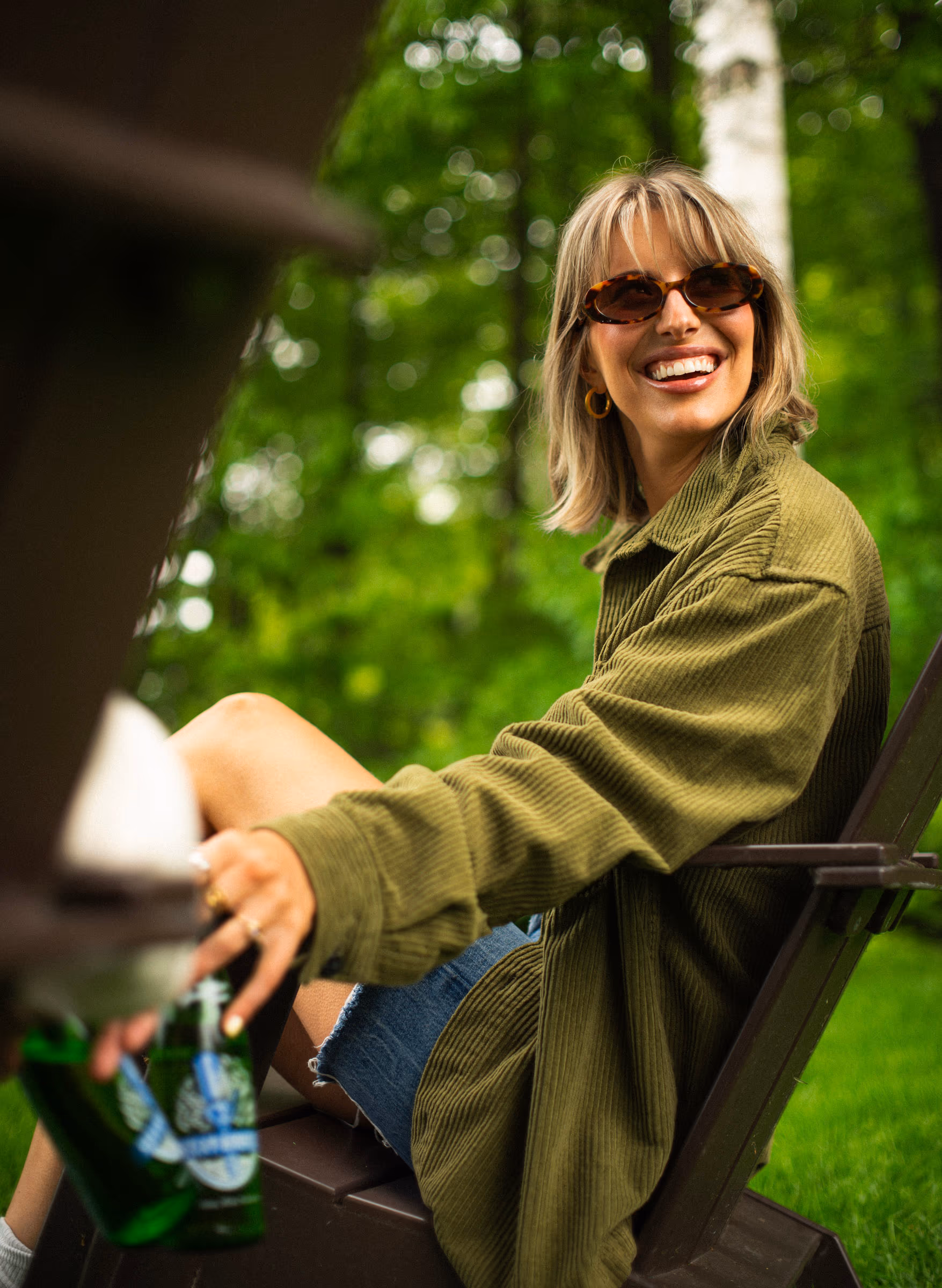 A woman in a Muskoka chair by the trees, Steam Whistle in hand