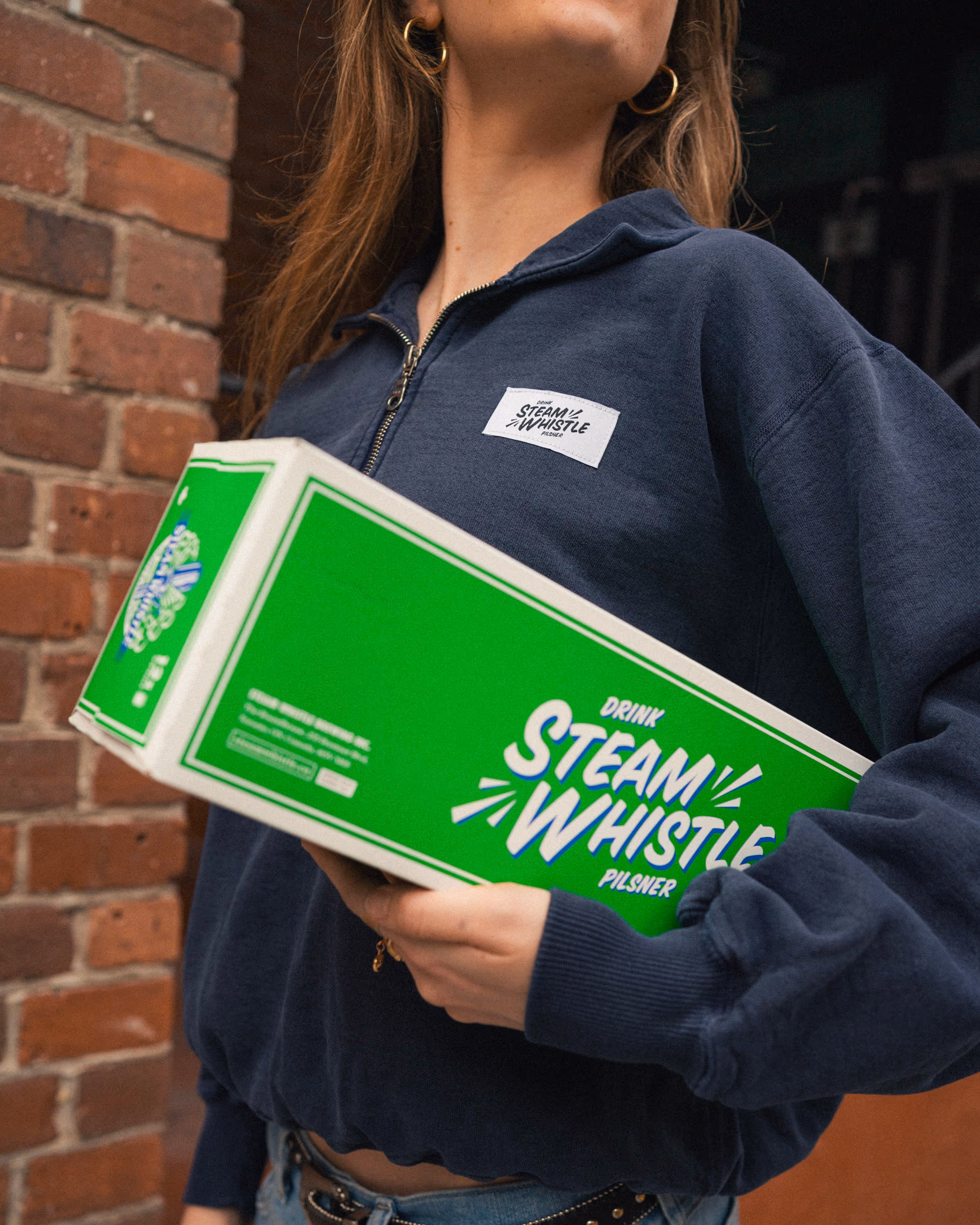 The 24-pack under an arm along the brick wall