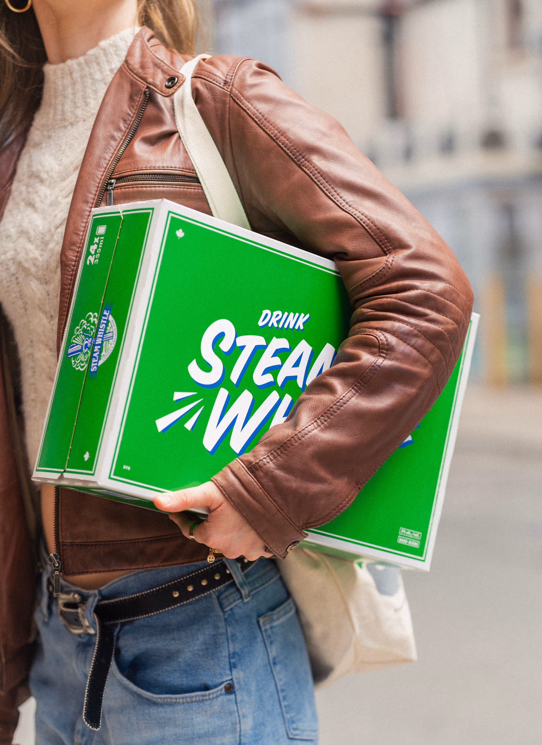 A woman in a leather jacket carrying a Steam Whistle 12-pack under her arm