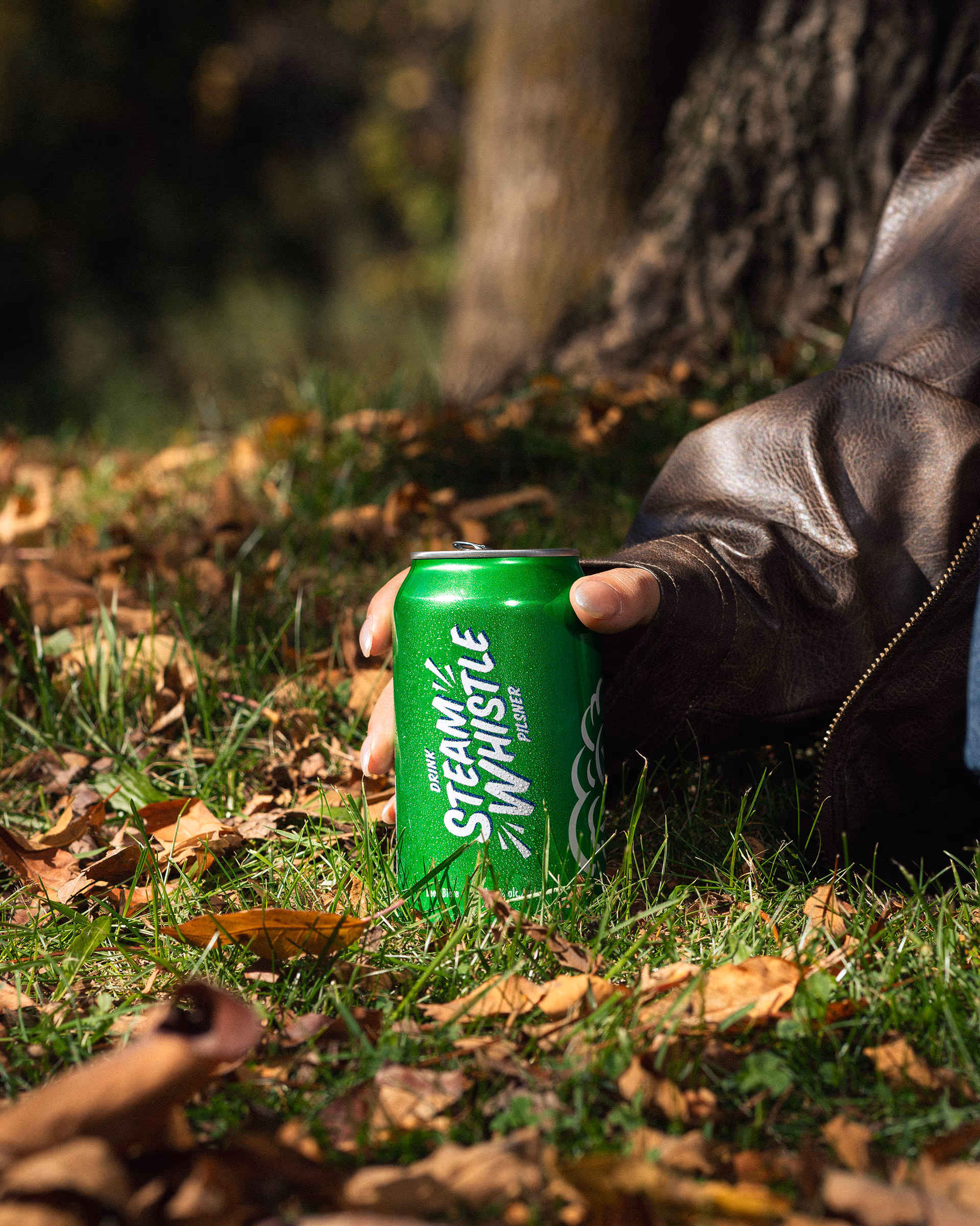 A leather-jacket hand holding a can among the leaves
