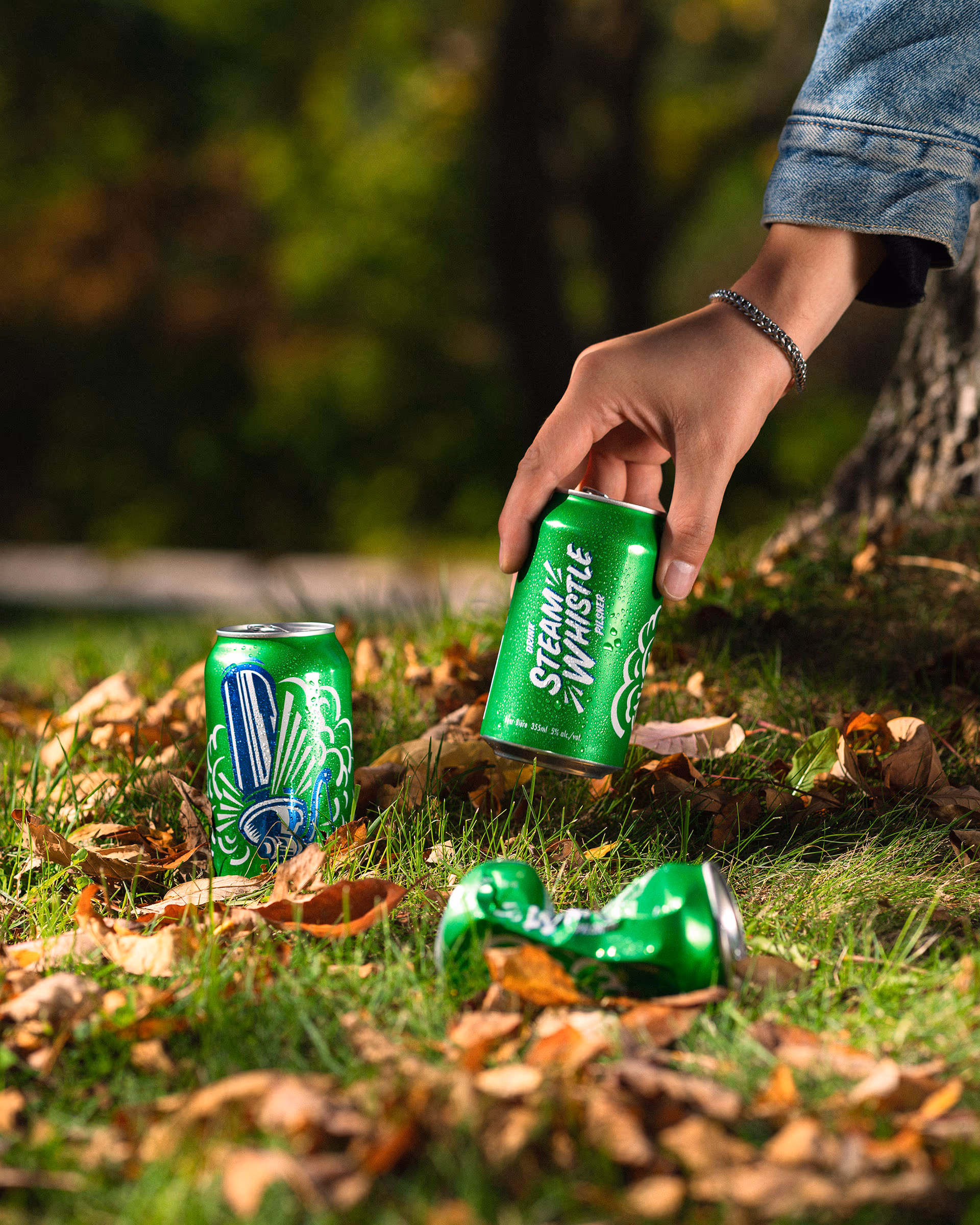 A hand pulling a Steam Whistle can from the fallen leaves