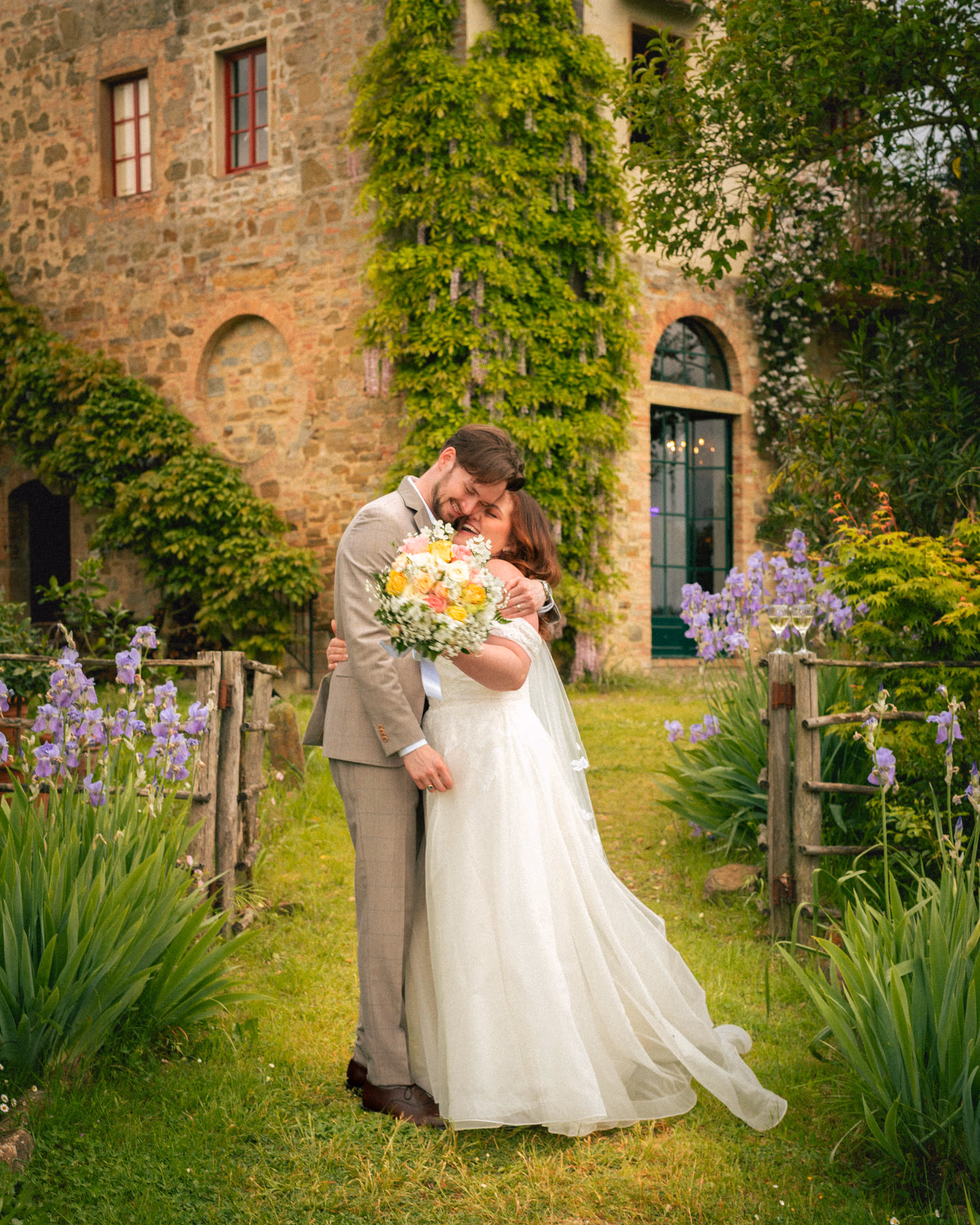 The couple embracing with the bouquet beside an ivy-covered stone wall