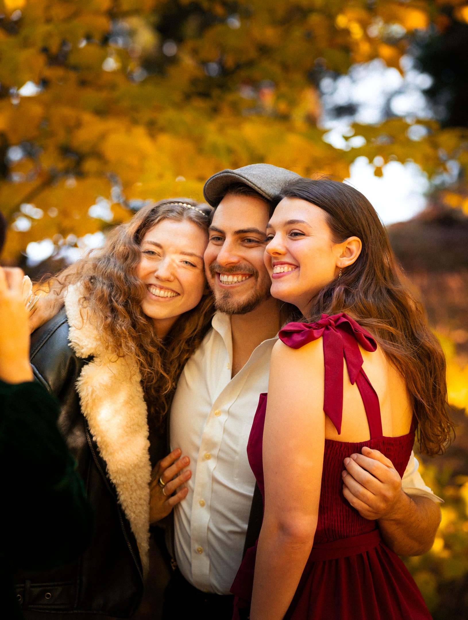 The couple laughing with a friend, cheek to cheek, in warm autumn light